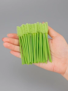 Close-up of disposable eyelash brushes with spiral bristles held in hand for scale