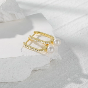 Macro shot of gold S925 silver U-shape earrings with white pearls and zircons on stone
