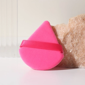 Borla de polvo triangular rosa con asa de cinta, situada sobre un fondo de piedra natural