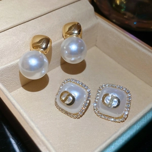 Detailed macro view of square pearl stud earrings with crystal halo and vintage gold CD logo