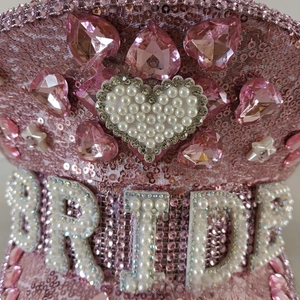 Close-up of pink sequin party hat with pearl BRIDE lettering and heart-shaped emblem
