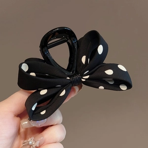 Pince à cheveux à nœud papillon à pois noirs et blancs tenue à la main pour femme