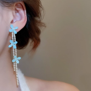 Detail of floral tassel earrings with blue flowers and pearls on model's ear