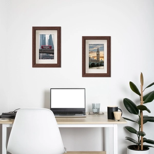 Modern brown wooden picture frames set on white wall above office desk with green plant