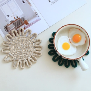 Detail of woven flower-shaped cotton trivets in beige and dark green on a table