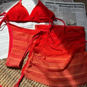 Flat lay of red three-piece crochet bikini set with wave texture on newspaper background