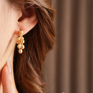 Detail of matte gold grape bunch earrings worn on model with soft lighting focus