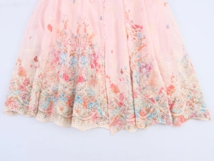 Detail van roze chiffonjurk met bloemenprint, parelknoppen en delicate kanten zoom