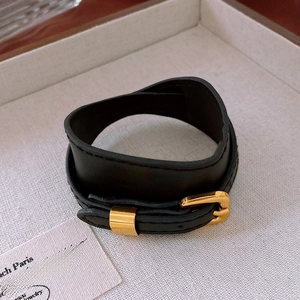 Detail of a minimalist black faux leather choker with adjustable gold metal buckle on wood