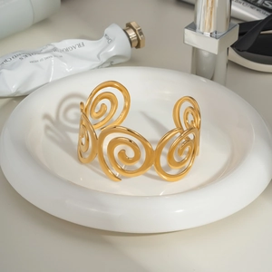 Detailed view of a gold spiral open cuff bracelet on a white ceramic display tray