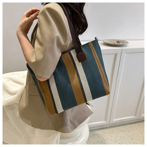 Detailed side view of a large striped canvas tote bag worn with a khaki blazer