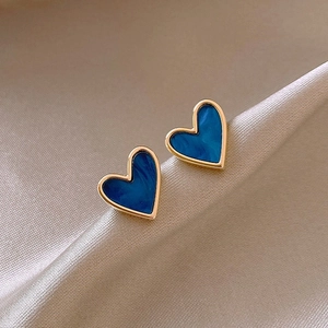 Close-up of heart-shaped gold earrings with dark blue enamel on champagne silk fabric