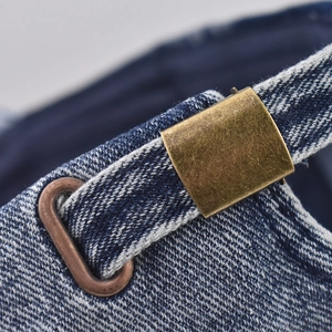 Detailed macro view of the vintage bronze buckle on washed blue denim baseball cap