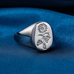 Macro shot of polished stainless steel signet ring with engraved sunflower on silk