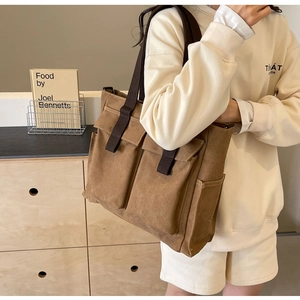 Close-up of brown canvas tote bag with large front pockets and stylish strap details