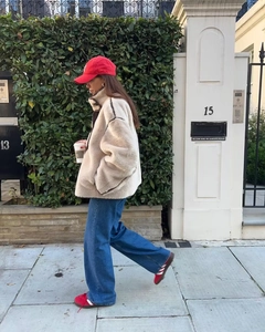 Detailansicht einer cremeweißen Fleecejacke mit blauer Jeans und roter Kappe