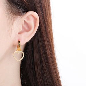 Détail de boucles d'oreilles cœur doré avec cristaux portées par un mannequin