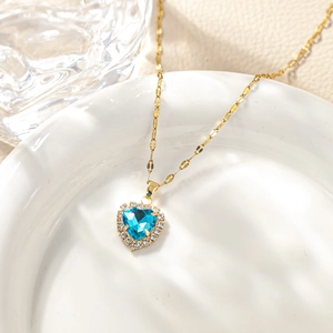 Macro detail of heart-shaped blue zircon pendant with gold chain on white ceramic