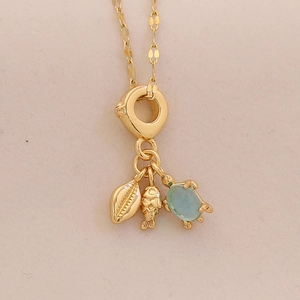 Detail of golden ocean necklace with turtle, shell and fish pendants on beige background