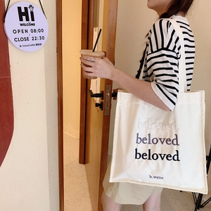 Détail de la broderie beloved sur un sac cabas en toile crème avec bandoulière longue