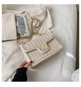 Detail of straw woven square bag with pearl trim, gold twist lock and chain strap