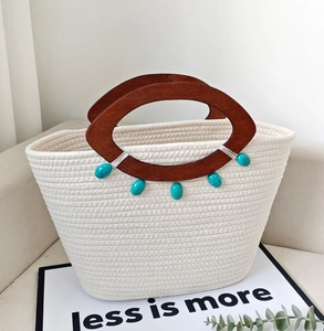 Detail of cream woven tote bag featuring brown wooden handles and turquoise bead accents