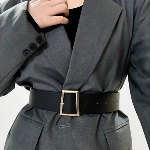 Detail of a black wide leather belt with a gold square buckle on a grey blazer jacket