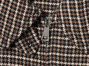 Macro shot of brown plaid jacket fabric with textured tweed and silver metal zipper
