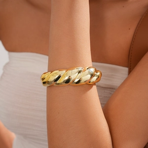 Detail of chunky gold twisted thread bracelet on wrist with textured metal finish