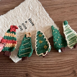 Five handmade knitted Christmas tree hair clips with embroidery on dark wood surface