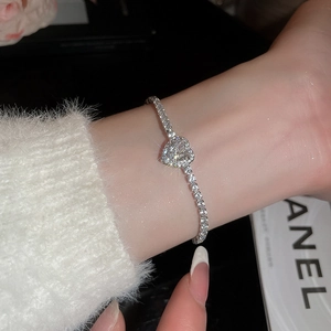Macro detail of a sparkling heart-shaped diamond bracelet on a wrist with faux fur