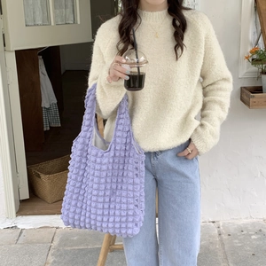 Detailed texture of purple bubble-textured tote bag carried by a model in a cafe setting