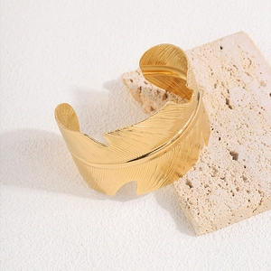 Detailed view of golden feather cuff bracelet with hollow leaf texture on travertine stone