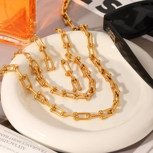 Detailopname van gouden U-schakel sieradenset met ketting en oorbellen op een wit bord