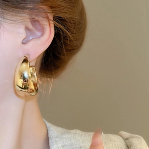 Close-up of polished gold C-shaped chunky earrings with reflective mirror finish on ear