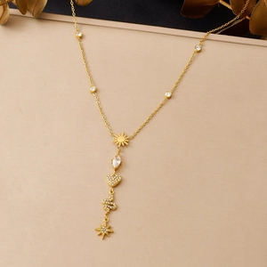 Detailed view of gold necklace with sun, heart, and snake charms on a textured stand