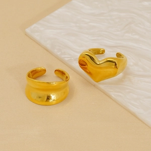 Minimalist gold heart and wavy irregular open rings set on a white marble surface