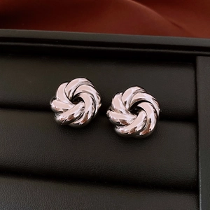 Macro shot of silver metallic swirl knot earrings on black jewelry display cushion