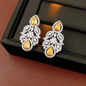 Close-up of silver earrings with yellow pear-cut stones and white zircon leaf patterns