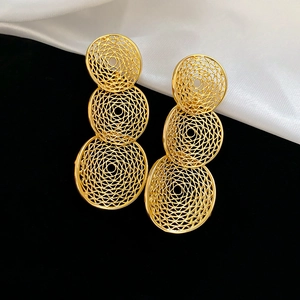 Detailed macro of gold-plated geometric hollow drop earrings on silk background