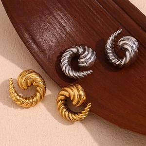 Macro detail of textured gold and silver spiral horn earrings on a premium wood surface