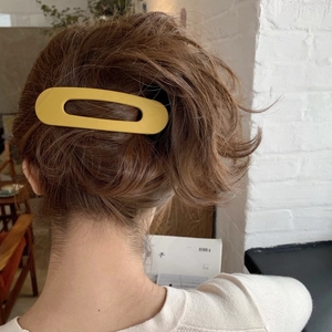 Detail of a matte yellow hollow oval hair claw clip worn by a model in a lifestyle setting