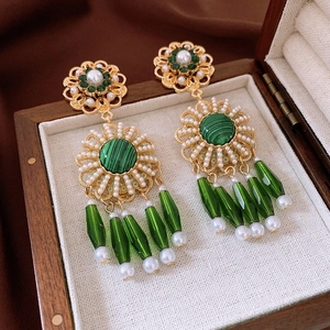 Close-up of gold flower earrings with green gems and pearls in a wooden jewelry box