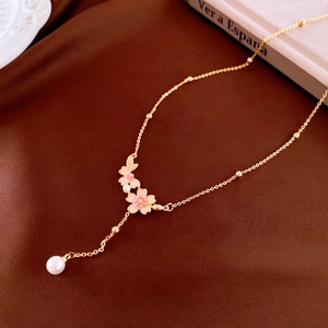 Detail of gold necklace with pink enamel cherry blossoms and elegant pearl pendant