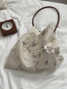 Detail of butterfly print canvas bag with slim brown handles on white bedding