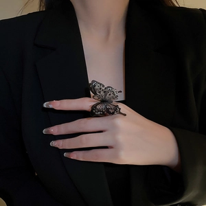 Detailed close-up of large black acrylic butterfly ring with glitter on a finger