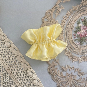 Detail view of yellow satin ruffled hair accessory with soft pleated texture and elegant shine