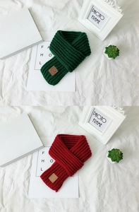 Detail of red and green knitted scarves with brown leather EST LOVE labels on white cloth