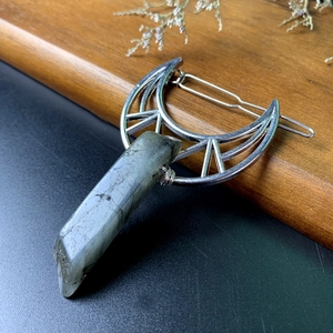 Close-up of silver crescent moon hair clip with a natural grey-green stone on wood