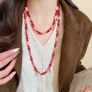 Detail of layered bohemian red bead necklaces on model in a stylish brown suit blazer